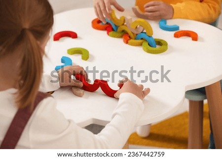 Little children playing with colorful wooden pieces at white table indoors, closeup. Developmental toy