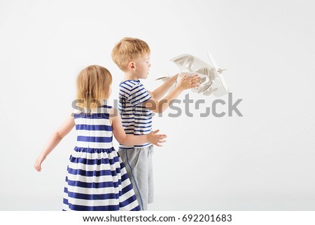 Little Children playing with paper toy airplane against a white background. Small Kids dreaming of becoming a pilot. Childhood. Fantasy, imagination.