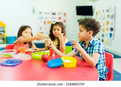 Little Children And Preschool Friends Sharing Their Food While Eating A Sandwich And Healthy Snacks During Lunch Break At School 