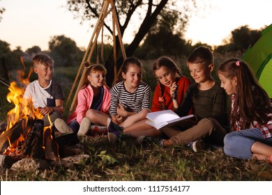 Little Children Reading Book With Flashlight Outdoors. Summer Camp