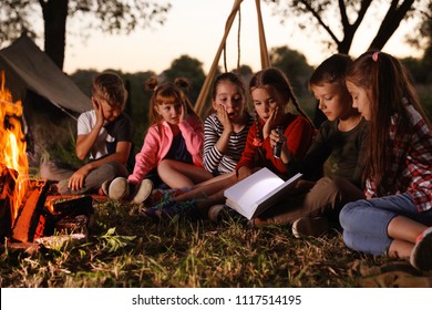 Little Children Reading Book With Flashlight Outdoors. Summer Camp