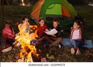 Little Children Reading Book With Flashlight Outdoors. Summer Camp