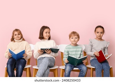 Little children reading books while sitting on chairs against pink background - Powered by Shutterstock