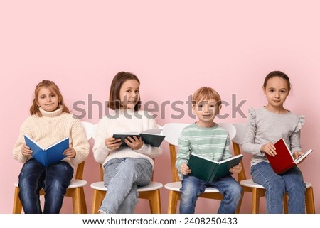 Little children reading books while sitting on chairs against pink background
