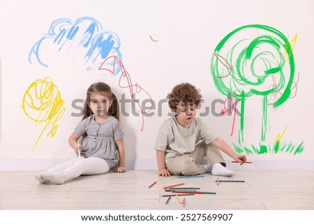 Little children sitting near white wall with drawings