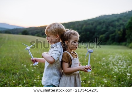 Little children standing in nature with model of wind turbine. Concept of ecology future and renewable resources.