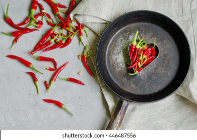 Little chili peppers in a heart shape on an iron frying pan on gray background, concept of hot love and passion