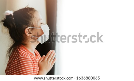 Little Chinese girl wearing mask for protect pm2.5 and coronavirus Covid-19.Stay at home praying to GOD.Online church worship in sunday.Little asian girl hand praying at home.Social distancing.