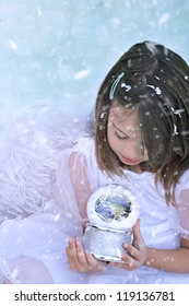 Little Christmas Angel In The Snow Holds A Snow Globe And Watches The Earth. Elements Of This Image Furnished By NASA.