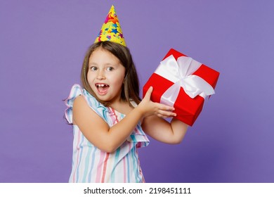 Little Cool Kid Child Girl 6-7 Years Old Wears Dress Birthday Hat Hold Red Present Box With Gift Ribbon Bow Isolated On Plain Pastel Light Purple Background. Mother's Day Love Family Lifestyle Concept