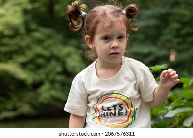 Little cool redhead girl with ponytails against the backdrop of a pond and a blurred green background