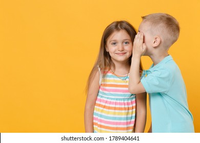 Little Couple Boy Girl 5-6 Years Old In Blue Pink Clothes Shirt Dress Have Fun Isolated On Yellow Background Children Studio Portrait. People Childhood Lifestyle Concept Whispering Secret Behind Hand.