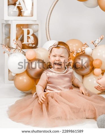 Little crying unhappy redhead baby girl celebrates first birthday anniversary. 1 year family party Professional photoshoot in photo studio. Cute adorable red hair kid in pink dress.Home children room.