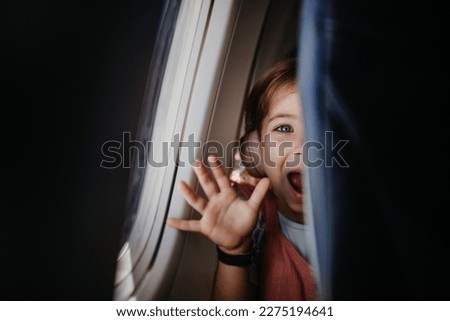 Little curious girl looking through seat in airplane.