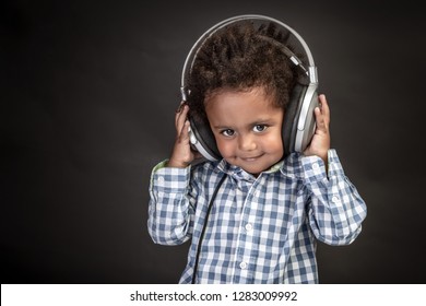 Little Curly African-American Baby Boy With Cute Smile Wearing Headphones, Sweet Child Having Fun And Listening Favourite Music, Black Background