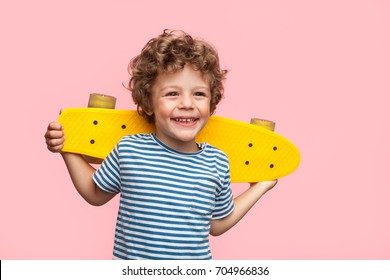 Little curly boy holding yellow longboard and looking away on pink background.  - Shutterstock ID 704966836