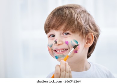 Little cute adorable child boy making a mess with colors on his face