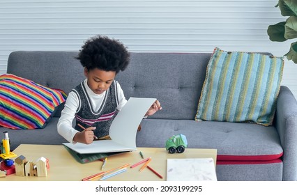 Little cute African black boy wearing casual sweater  sitting alone in cozy living room at home weekend  writing  doing homework  drawing picture and happiness  Kid  diversity  Education Concept