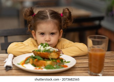 Little Cute Angry Girl Sitting At Table In Restaurant, Against Breakfast.Child Kid Have France Lunch Outdoors. Concept Of Eco Healthy Food.