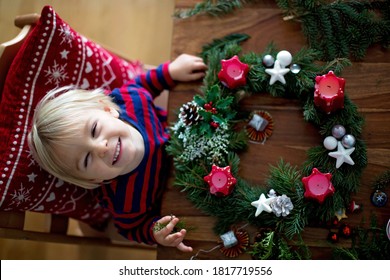 Little cute blonde toddler boy, making advent wreath at home, decorating it