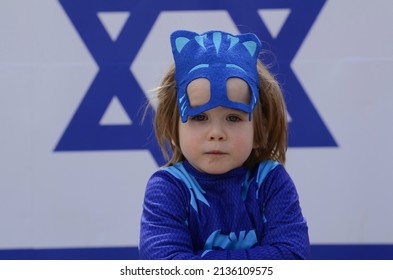 Little Cute Boy With Blond Hair In A Carnival Costume On The Background Of The Flag Of Israel. Jewish Holiday Purim. Child In Catboy Costume