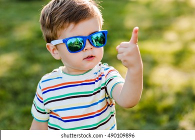 Little Cute Boy In Bright Sunglasses Shows Number One In Summer Garden