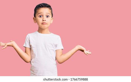 Little cute boy kid wearing casual white tshirt clueless and confused expression with arms and hands raised. doubt concept. 