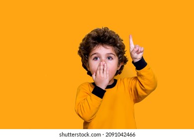 Little Cute Boy Kid Wearing School Bag And Holding Book Covering Mouth With Hand. Shocked And Afraid For Mistake Face. Portrait Of Surprised Expression