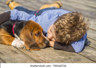 Little Cute Boy Is Sitting By The River With His Dog. They Enjoy Together On A Beautiful Sunny Day. Boy Hugging His Puppy. Growing Up, Love For Animals - Dogs, Free Time, Travel, Vacation. Copy Space