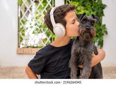 Little Cute Boy Is Sitting With His Dog. They Enjoy Together On A Beautiful Sunny Day. Boy Listening To Music Via Headphones. Growing Up, Love For Animals. 