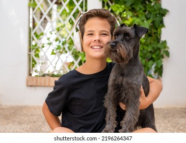 Little Cute Boy Is Sitting With His Dog. They Enjoy Together On A Beautiful Sunny Day. Boy Listening To Music Via Headphones. Growing Up, Love For Animals. 