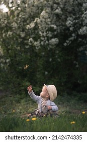 Little cute boy in a stylish hat with a toy bike playing with a butterfly on a green meadow on a warm spring day. Portrait of a child in profile with copy space
