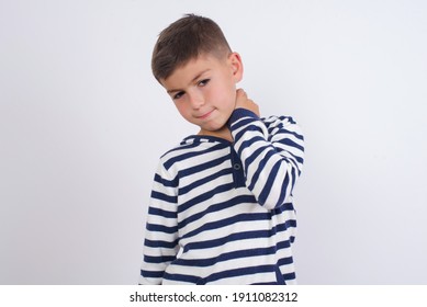 little cute Caucasian boy kid wearing stripped t-shirt against white wall suffering from back and neck ache injury, touching neck with hand, muscular pain.