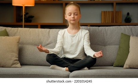 Little Cute Caucasian Girl Young Healthy Child Blonde Kid Preschooler Meditate Sit On Sofa At Home Calm Mindful Peaceful Daughter Do Yoga Breathing Exercise Relax Alone With Closed Eyes In Lotus Pose