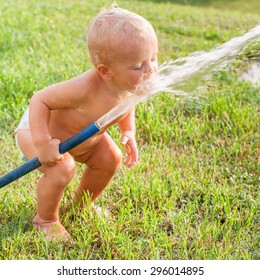 Little Cute Child Boy Playing With A Rubber Hose In The Garden