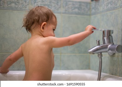 a little cute child, while bathing in the bath, plays with a water tap, turns it on and off. against the background of a green bathroom in blur close-up, soft focus