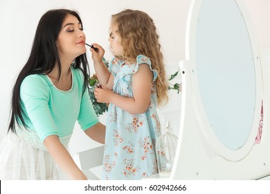 Little cute daughter and her mother applying make up each other. Pretty young mom and adorable girl having fun together. Beautiful fashionista family - Powered by Shutterstock