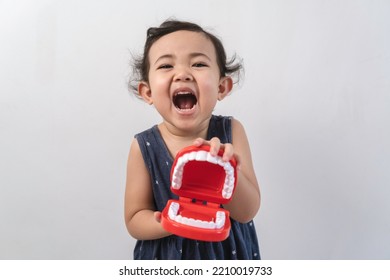 Little cute funny asian girl holding tooth jaw.Kid training oral hygiene. Child learning brushing, cleaning teeth. Prevention of caries in children. children dentistry. dental care kids - Shutterstock ID 2210019733