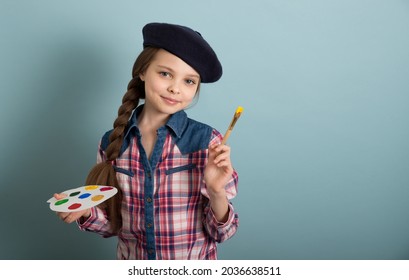 Little cute girl artist poses in the studio with paints, a brush and a palette in her hands. Kid and arts. Children hobby concept.