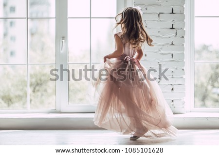 Little cute girl in beautiful dress is dancing near the window at home.