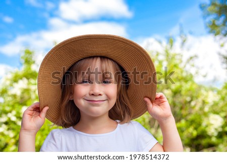 Little cute girl in a big hat on the background of trees and sky.