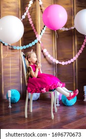 Little cute girl with blond hair in a pink dress and a princess crown with large bright balloons and garlands. Children's holiday. Children's decor. Balloons