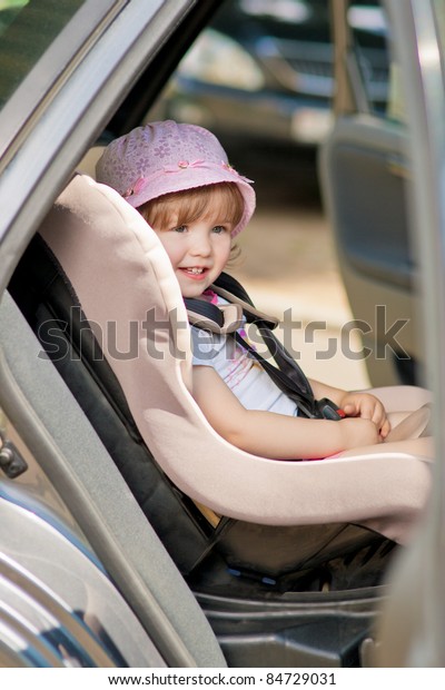little cute girl in cap sitting in the car in\
child safety seat and\
smiling