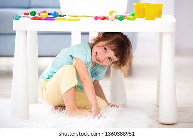 Little Cute Girl Crawled Under The Table. The Kid Smiles, Plays Hide And Seek