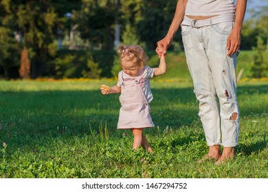 Little cute girl does her first steps with mother support, green grass, summer time, soft focus background