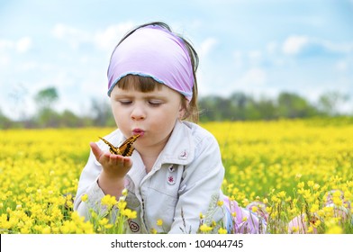 Little cute girl in a field of beautiful yellow flowers holding a butterfly on the palms and blowing on it.