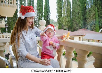 Little Cute Girl And Her Young Mother In Santa Hats In Tropical Country Hotel Balcony. Waiting For Santa. Happy Holidays. Stay Home, Covid, Coronavirus, Merry Christmas. New Year Concept