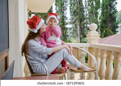 Little Cute Girl And Her Young Mother In Santa Hats In Tropical Country Hotel Balcony. Waiting For Santa. Happy Holidays. Stay Home, Covid, Coronavirus, Merry Christmas. New Year Concept