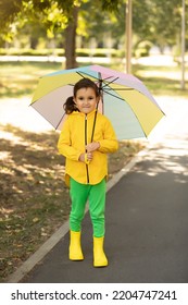 Little Cute Girl Kid Child In A Yellow Raincoat With Multicolored Rainbow Umbrella Laughs And Looks At Camera