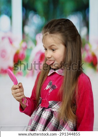 Little cute girl with long hair shows her tongue in mirror